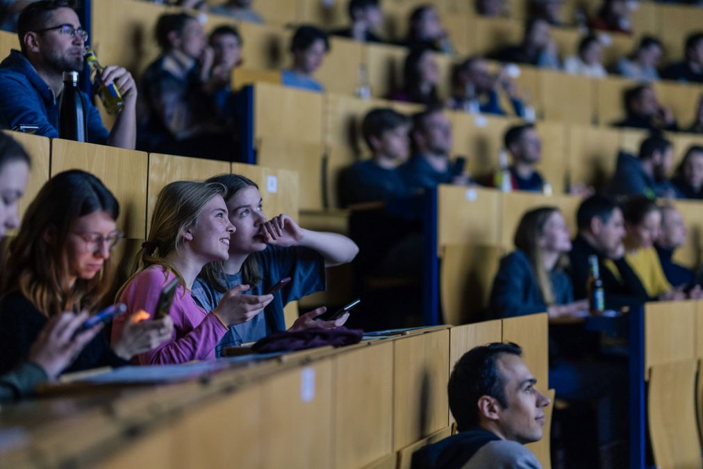 zur Vergrößerungsansicht des Bildes: Mehrere Personen in einem Hörsaal nutzen ihre Handys. 