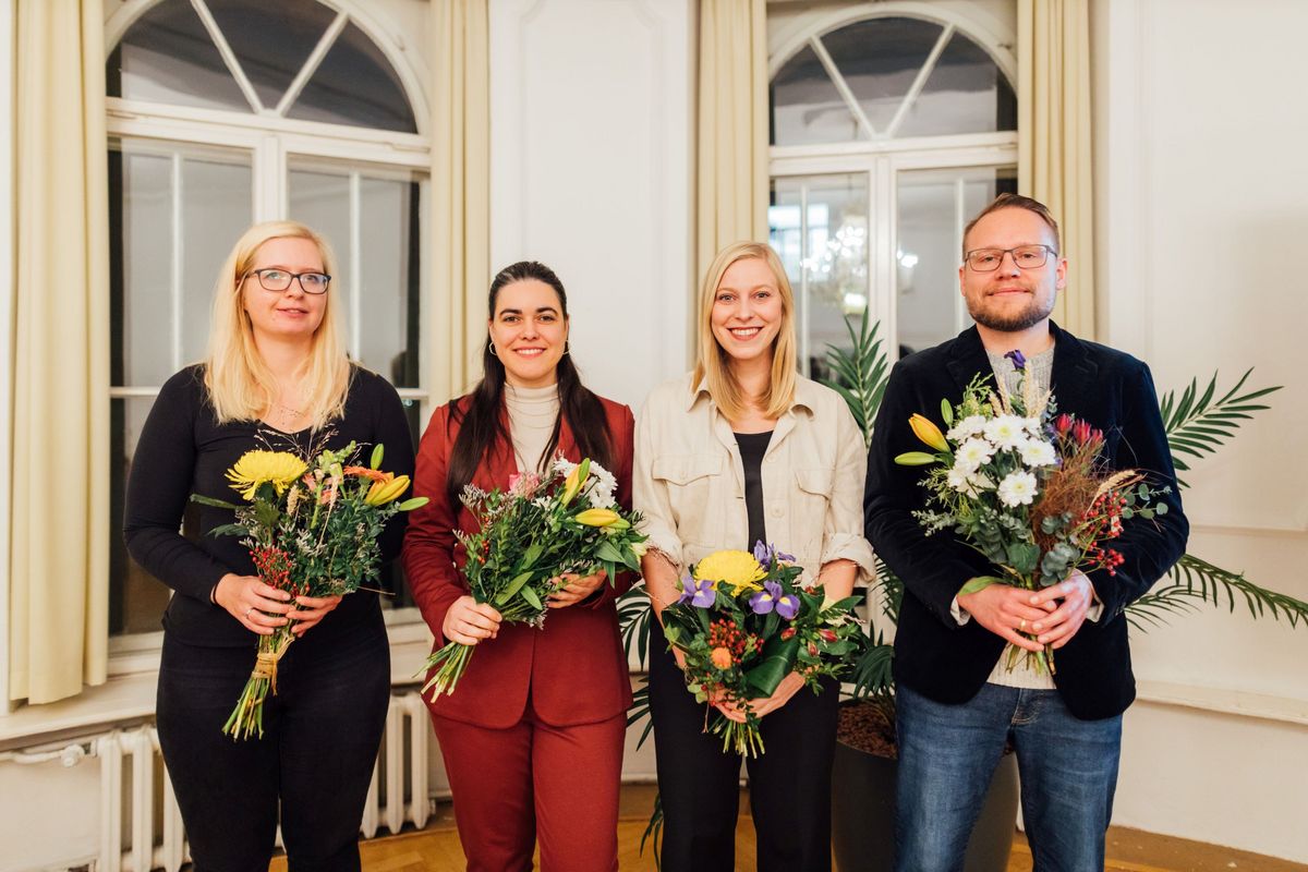 zur Vergrößerungsansicht des Bildes: Vier Preisträger:innen posieren mit Blumen in der Hand