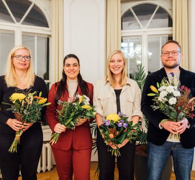 Vier Preisträger:innen posieren mit Blumen in der Hand